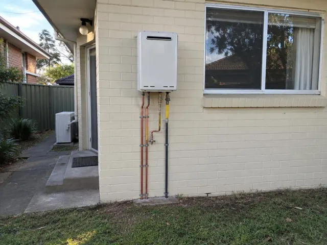 Wall-mounted hot water unit on a cream brick exterior wall beside a window in Eastlakes